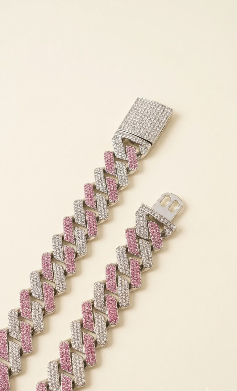 A close-up of a silver-toned chain bracelet with alternating rows of pink and clear rhinestones, laid diagonally on a light cream background.