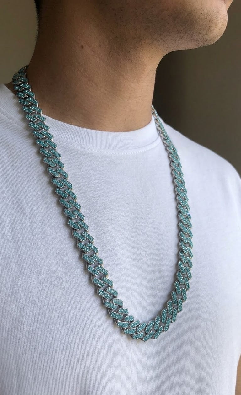A close-up of a person wearing a chunky, textured chain necklace in a muted teal-green color over a white t-shirt.