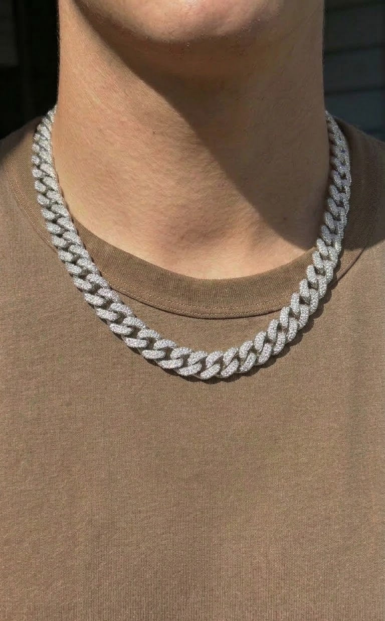 A close-up of a person wearing a thick silver-toned Cuban link chain necklace over a brown t-shirt.