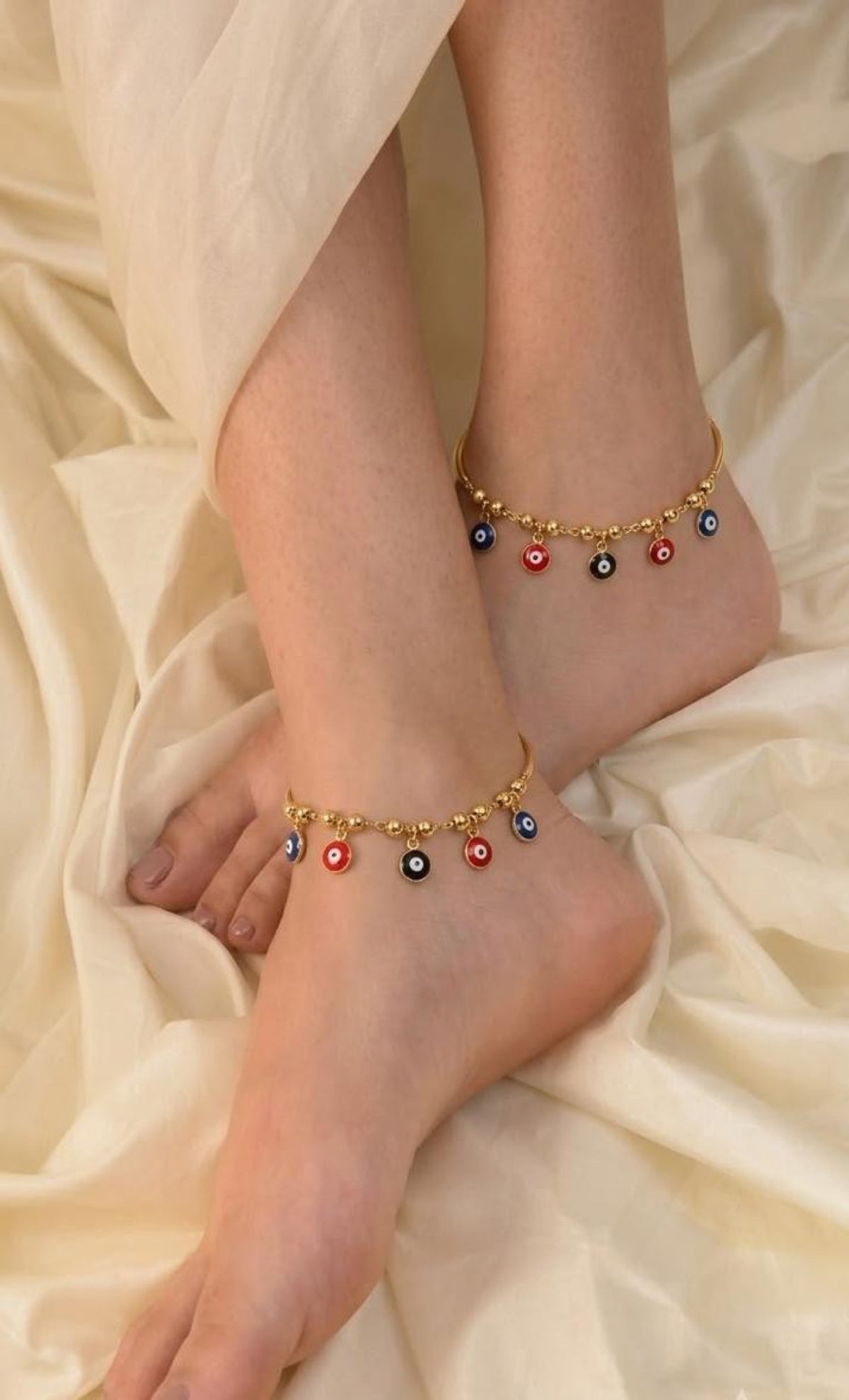 Pair of gold-tone anklets with curved bars and blue, red and black evil eye drops